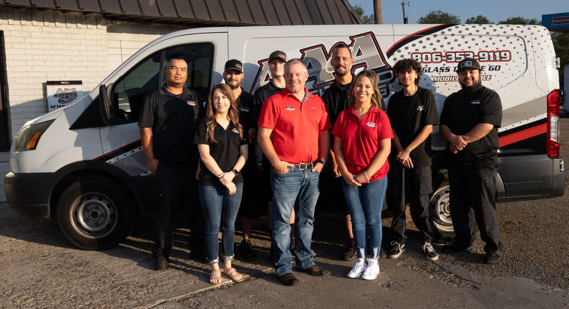 Group posing in front of a white van, with two people in red shirts at center.