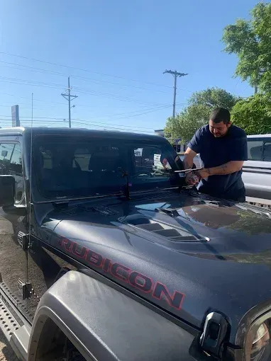 Man cleaning a black Jeep with red lettering outdoors in bright sunlight.
