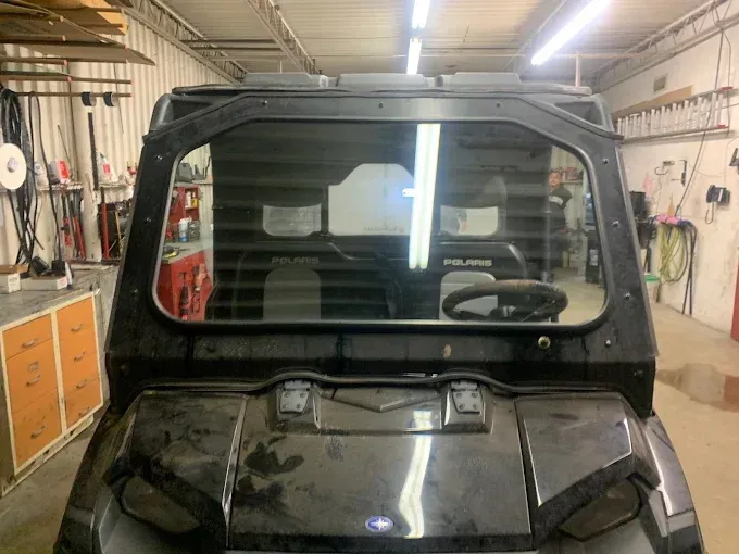 Black off-road vehicle in a workshop garage, viewed from the front with tools and cabinets in the background