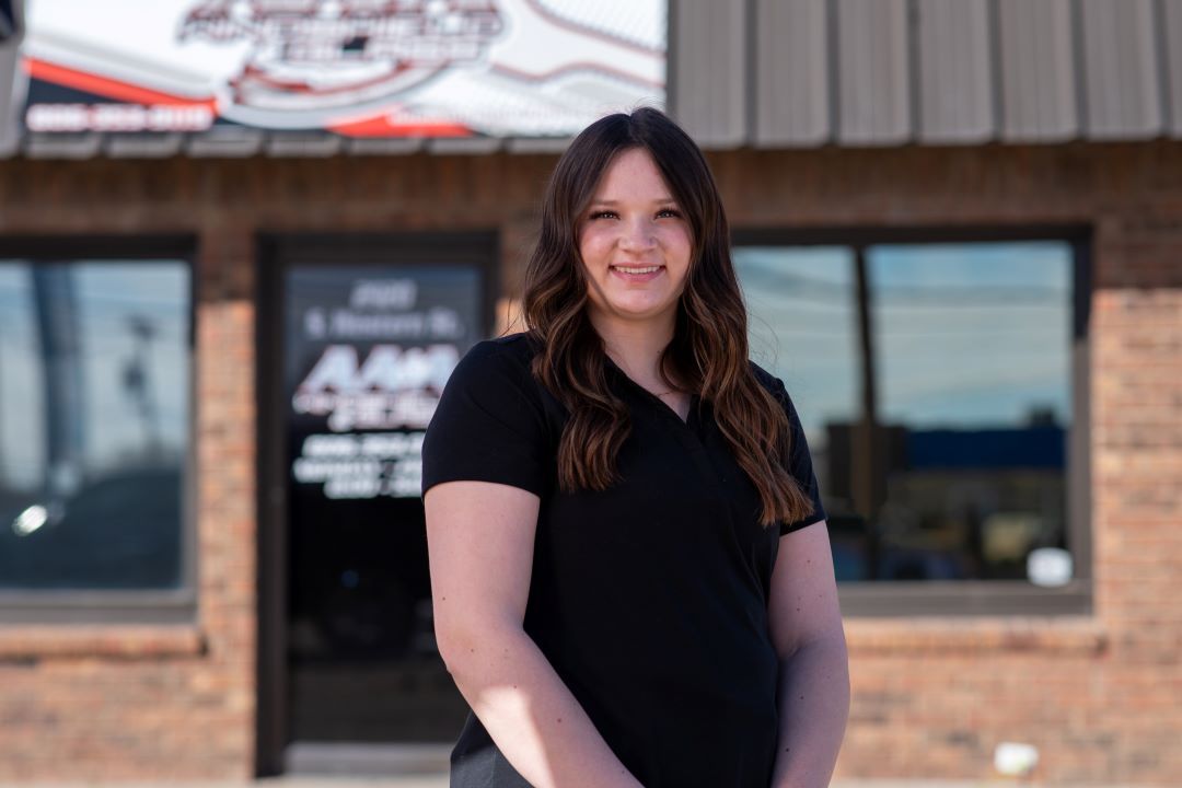 Woman standing outside a brick building, smiling, in a black shirt.