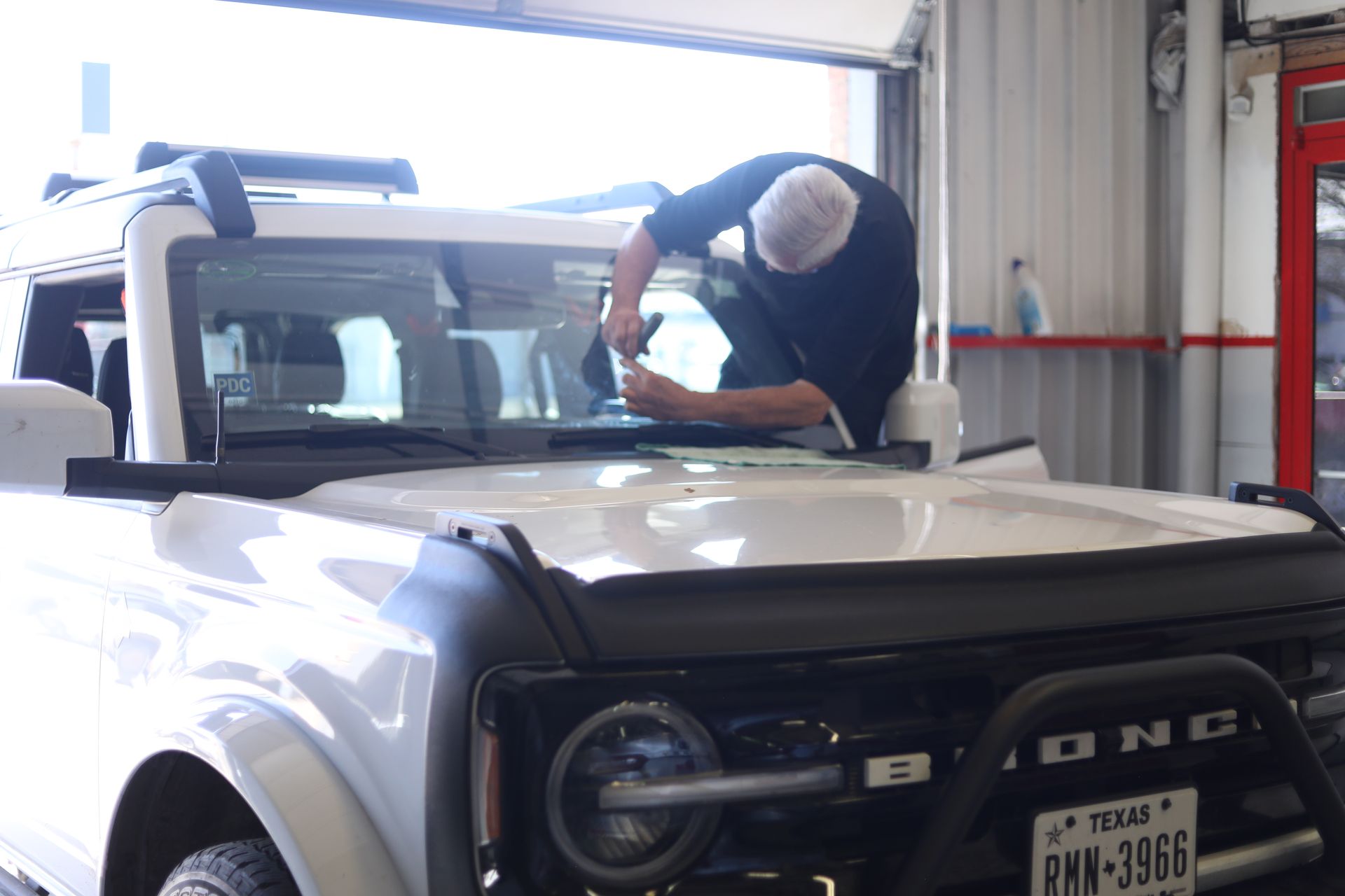 Person cleaning the windshield of a white Ford Bronco in a garage.
