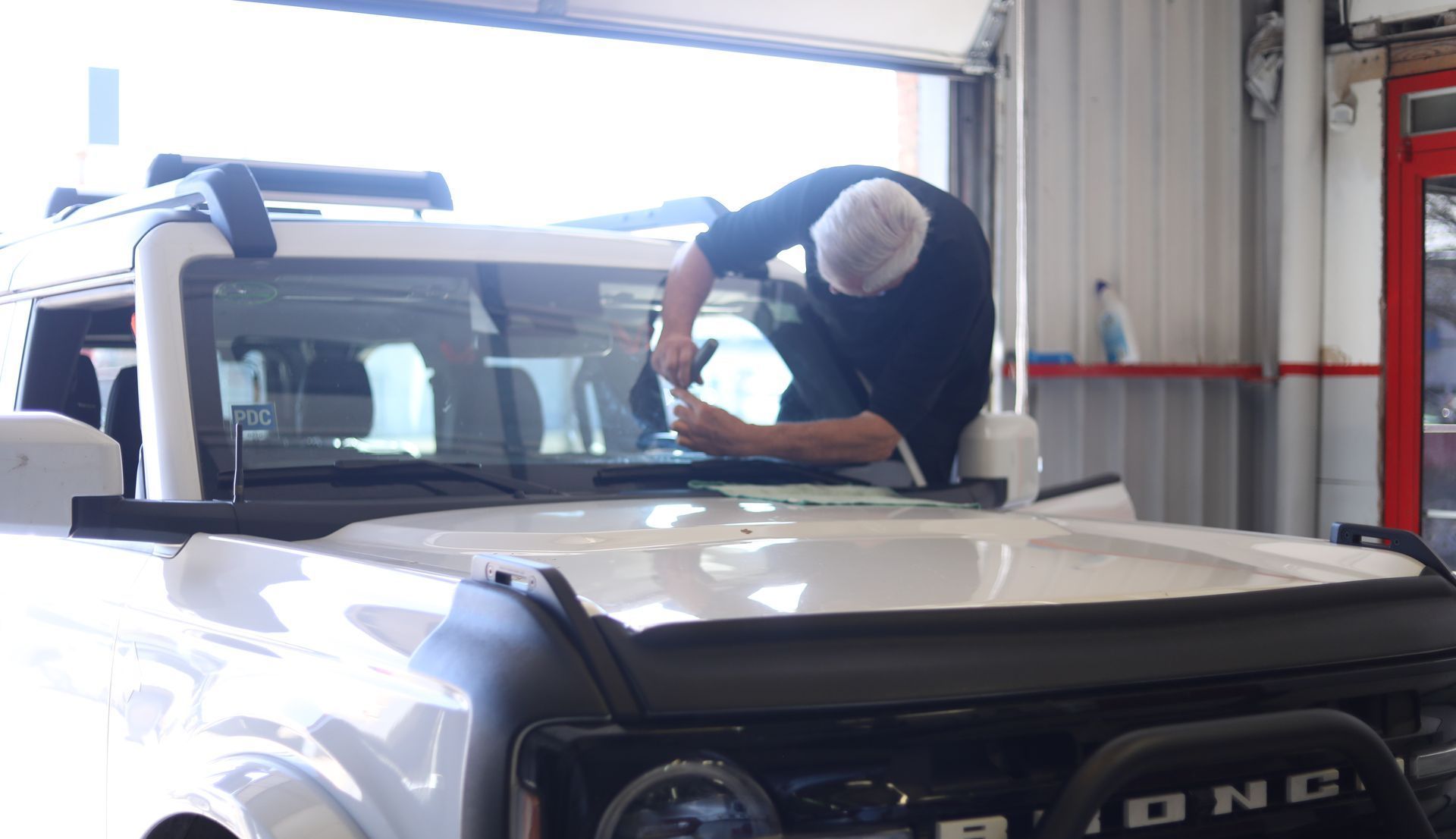 Person cleaning the windshield of a white Ford Bronco in a garage.