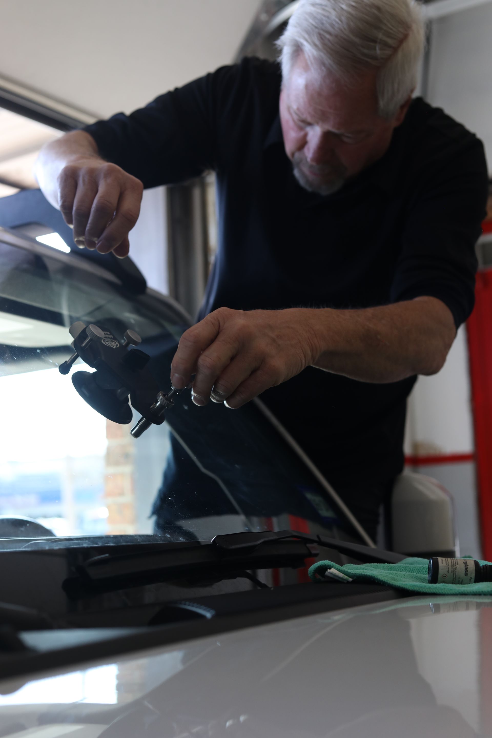 Man leaning over a car windshield, installing or adjusting a wiper blade indoors