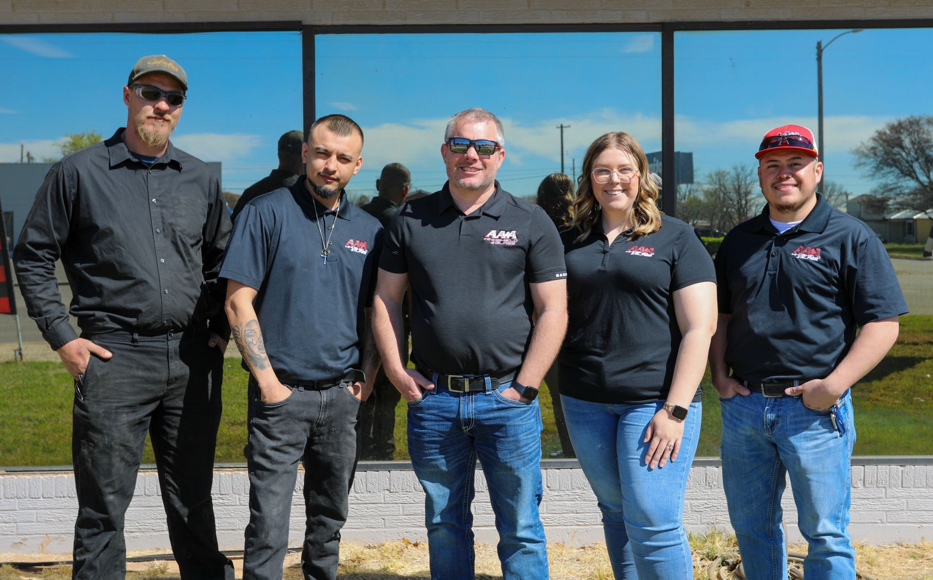 Five coworkers standing outside a building, wearing black shirts and jeans, posing in sunlight.