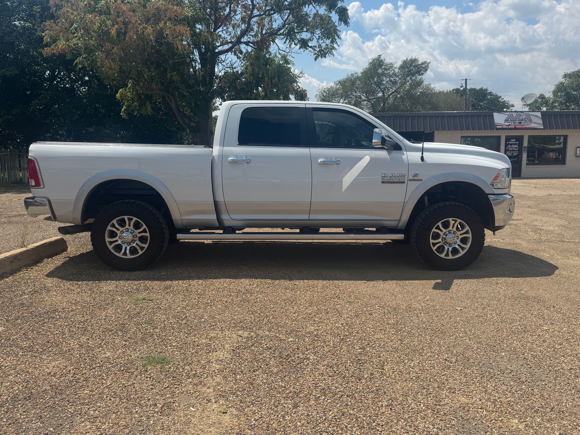 White pickup truck parked on a gravel lot with trees and buildings in the background