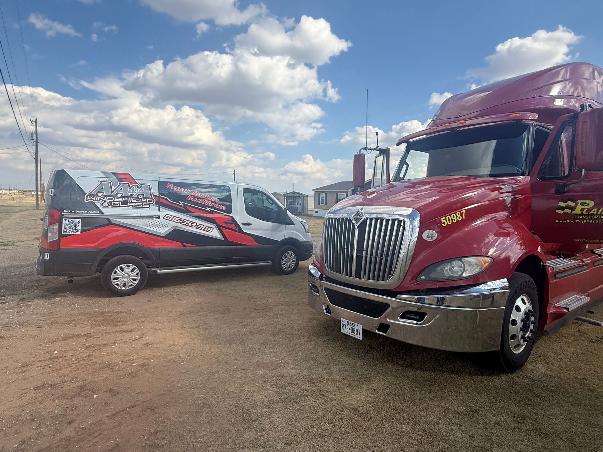 Two red commercial trucks parked on a dirt lot under a cloudy sky.