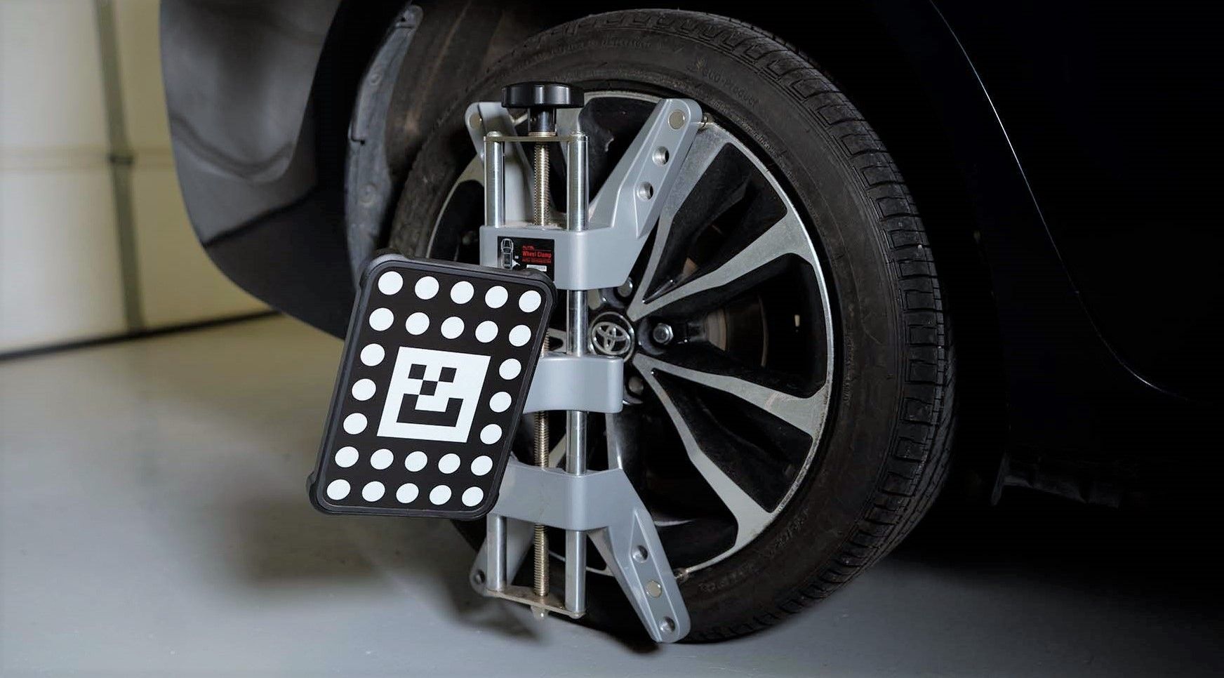 Wheel alignment machine clamped to a car tire in a garage, with a black calibration target panel