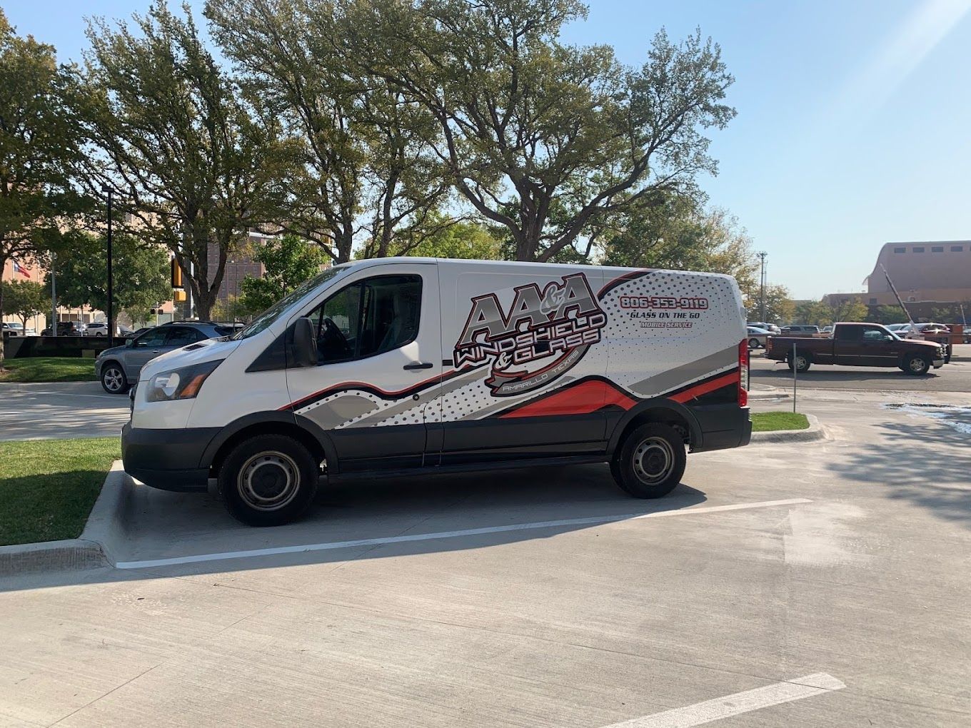 White delivery van with red and black graphics parked in a lot beside trees on a sunny day