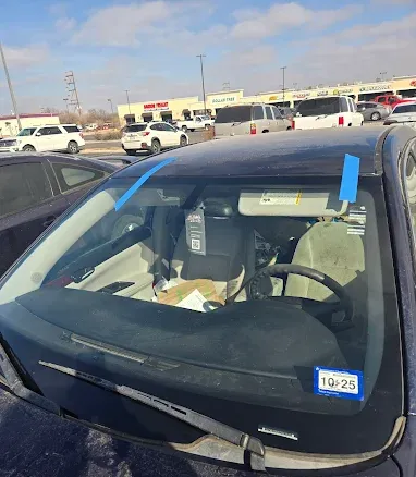 Damaged car windshield with blue tape in a parking lot on a sunny day