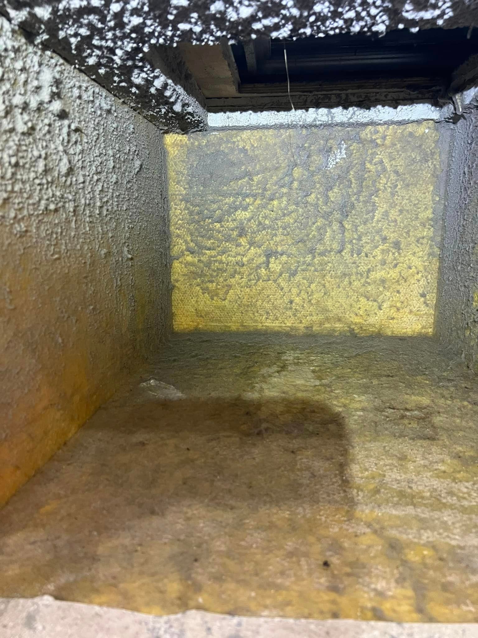 Empty industrial tank interior with yellow-brown residue on the floor and walls, viewed through an open hatch
