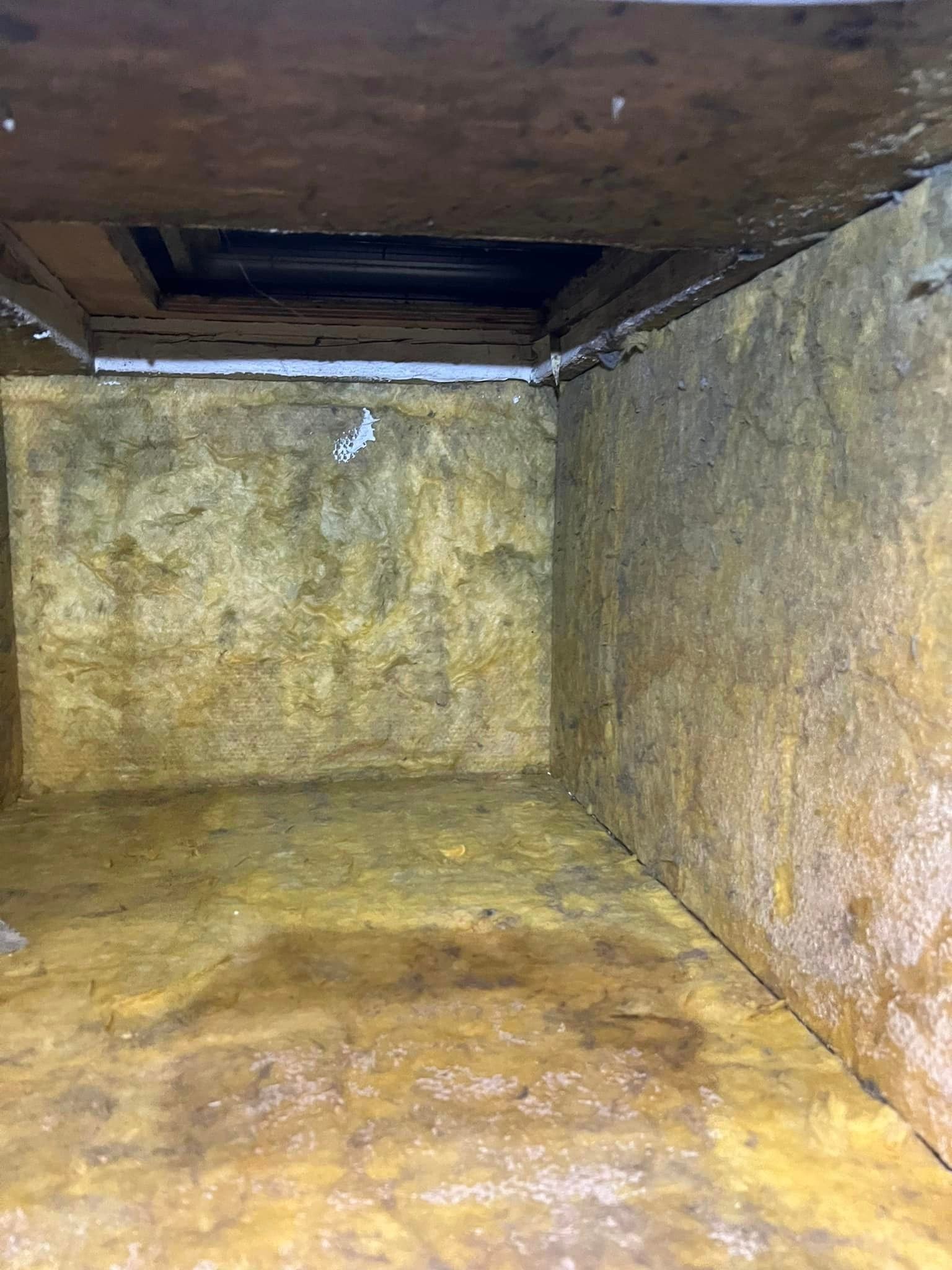 Empty yellow-stained metal duct or vent interior with dark opening at the top.
