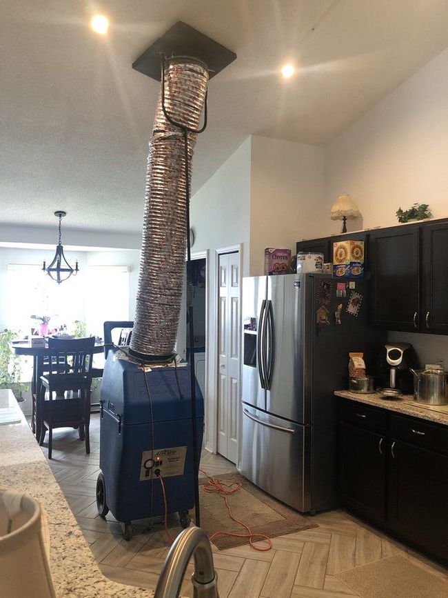 Portable air conditioner with duct hose in a kitchen beside a stainless refrigerator and black cabinets.
