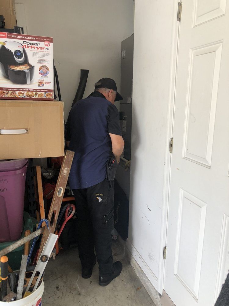 Person working beside a white door in a narrow storage area, surrounded by tools and household items