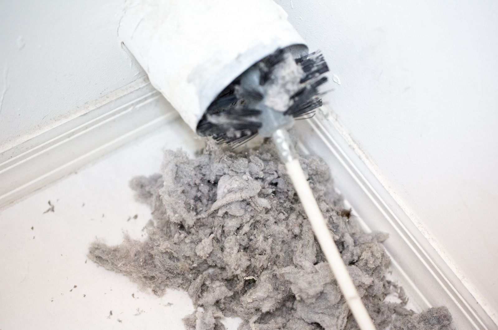 Cleaning a dryer vent: a brush removes a large pile of lint from inside the vent.