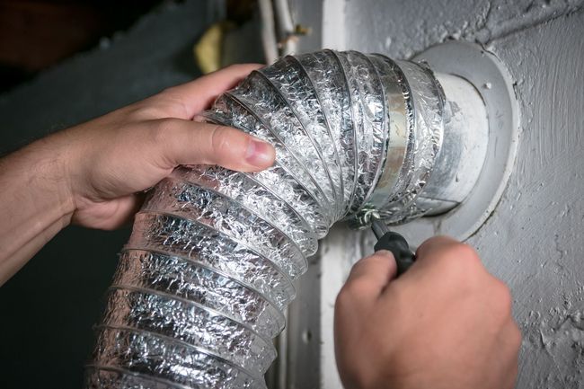 Hands securing a silver flexible duct to a wall vent with a screwdriver
