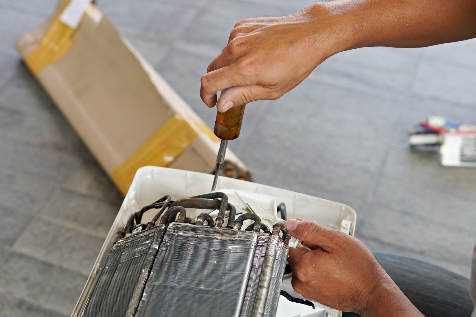 Hands repairing a white appliance with a screwdriver on a tiled floor