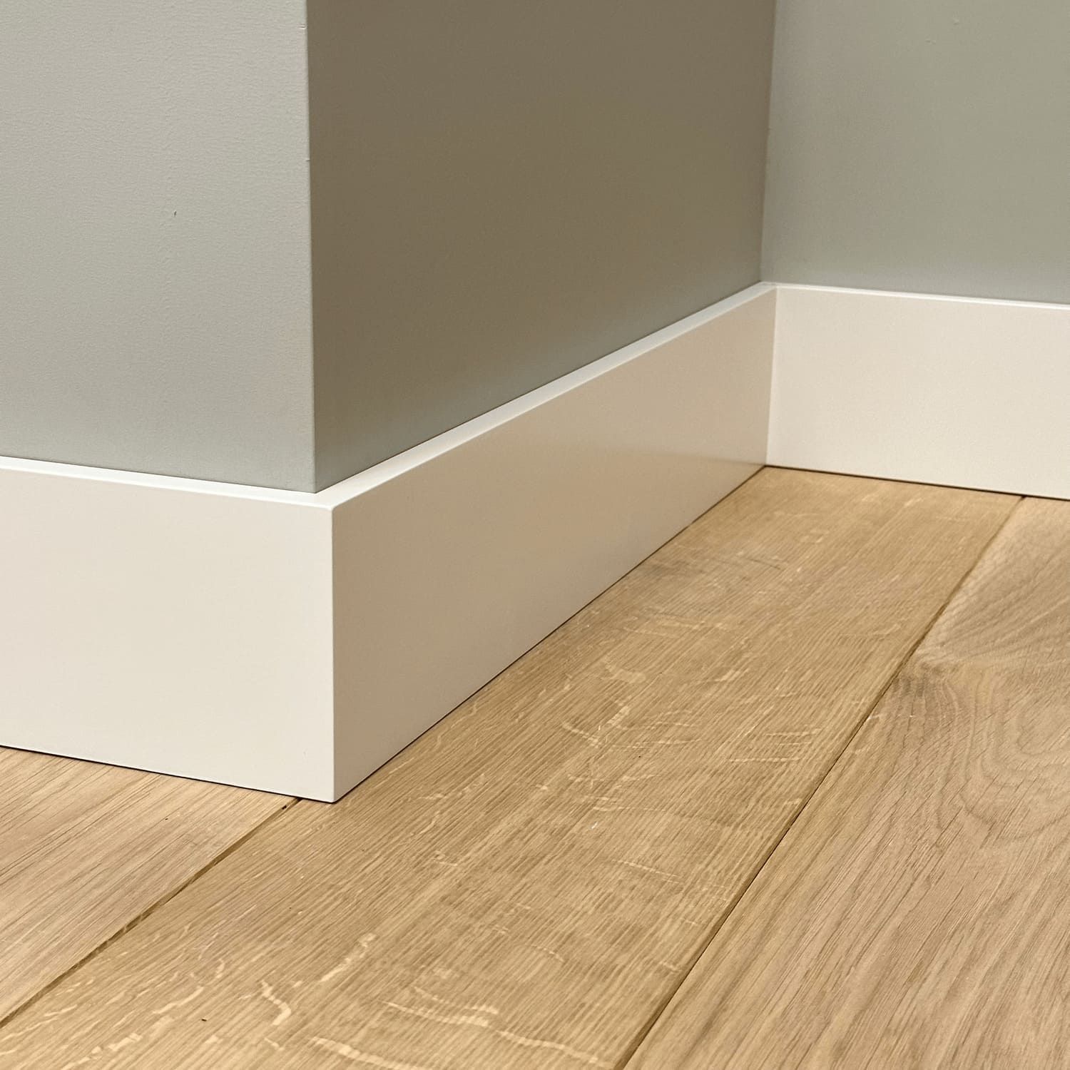 Een close-up van een witte plint op een houten vloer.