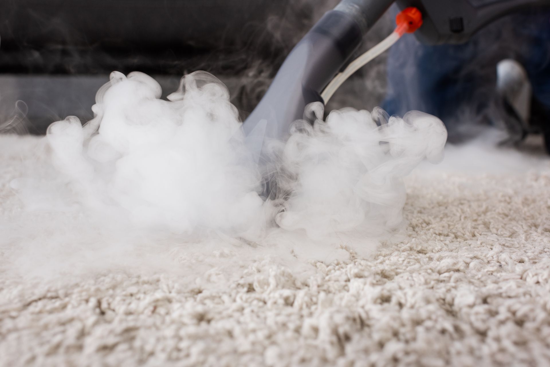 Steam cleaning nozzle spraying thick white vapor over a carpeted floor