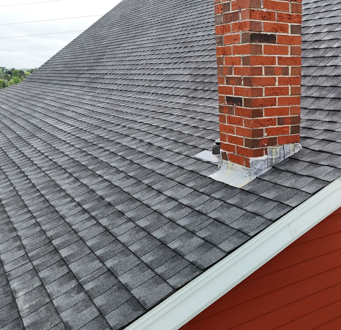 Gray shingle roof with a brick chimney and white trim; red house siding.