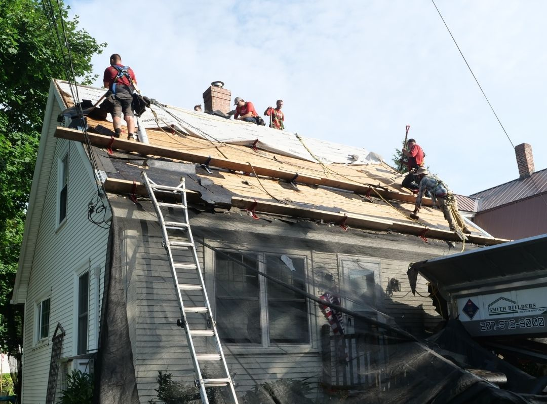 Roofers working on a residential roof, removing old shingles and preparing for repairs.