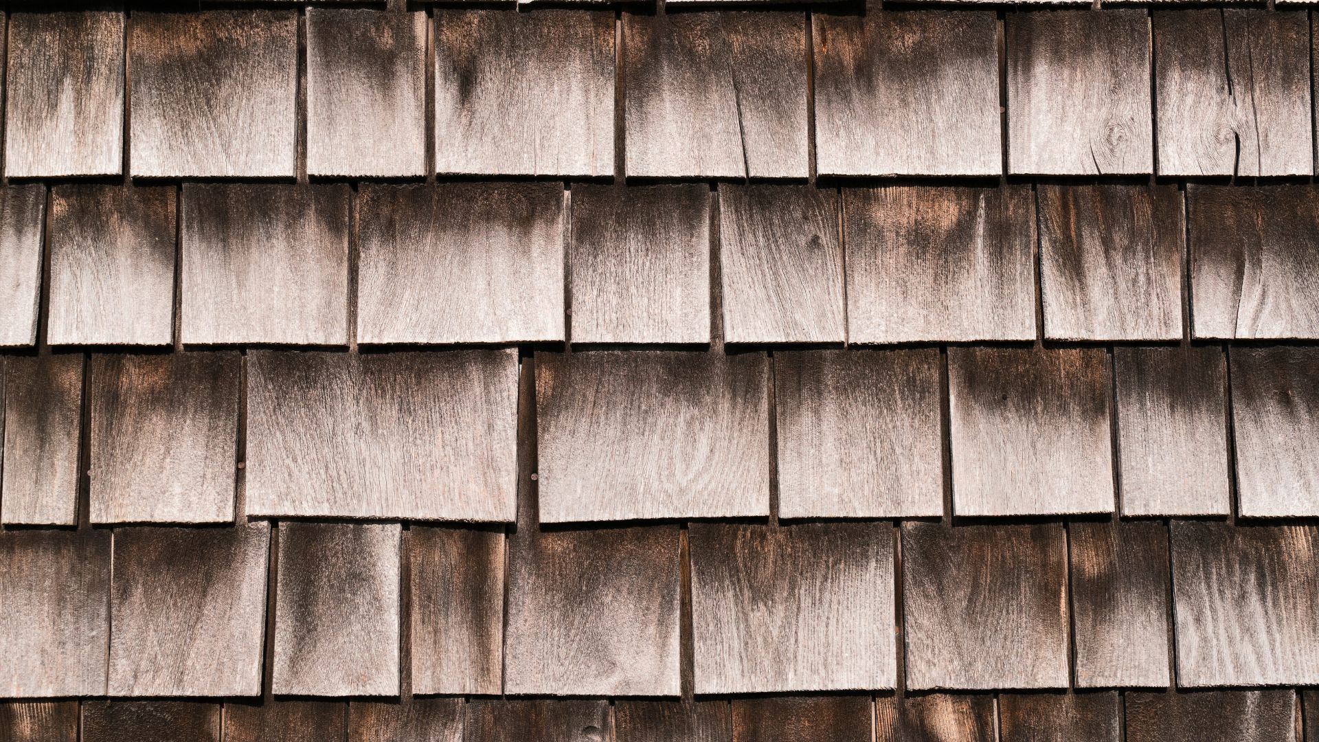 Stacked beige and tan wooden shingles arranged in horizontal rows on a wall.