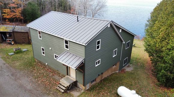 Green house with metal roof by a lake.