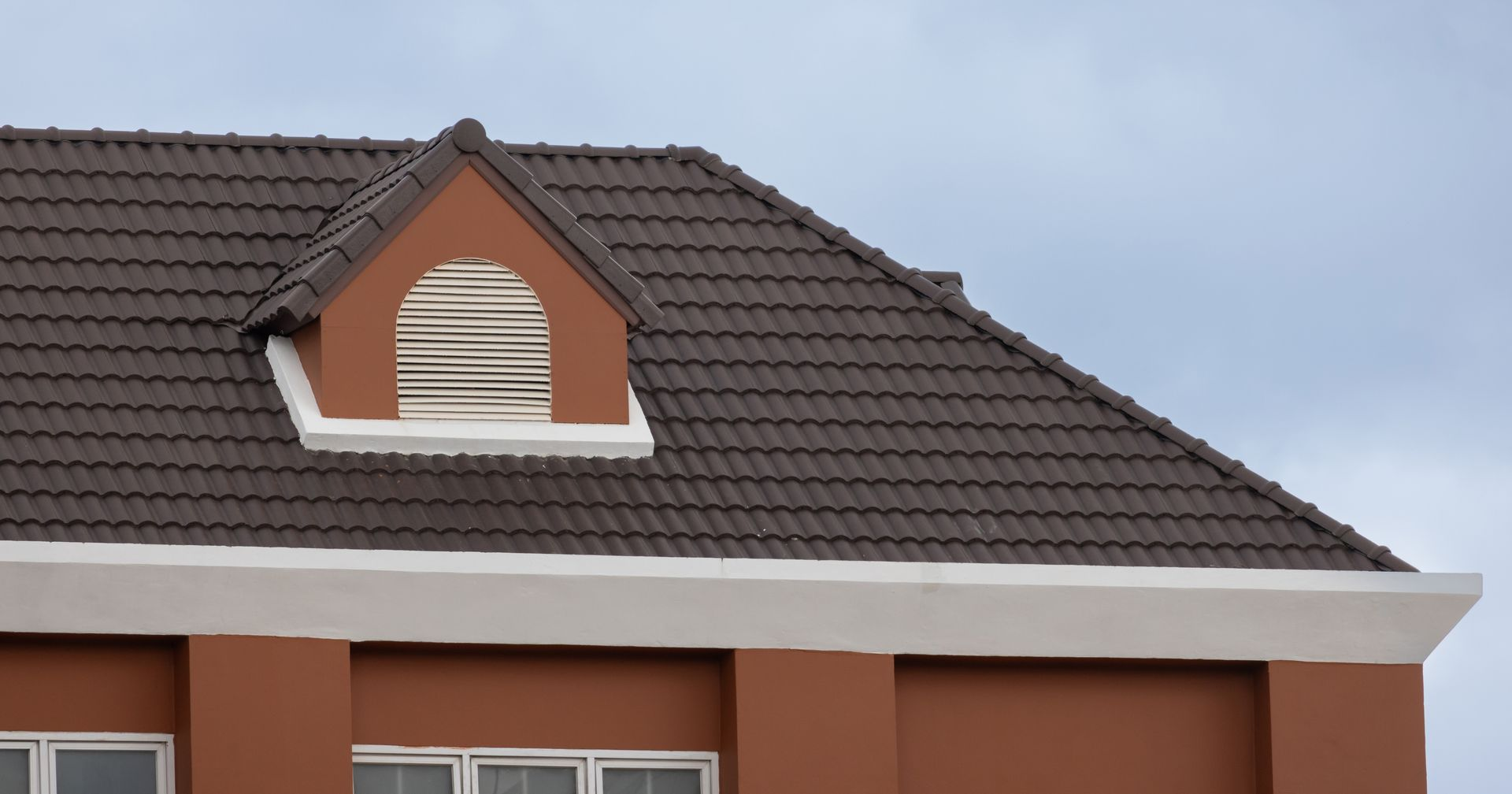 House roof with brown tiles and a small dormer window against a cloudy sky
