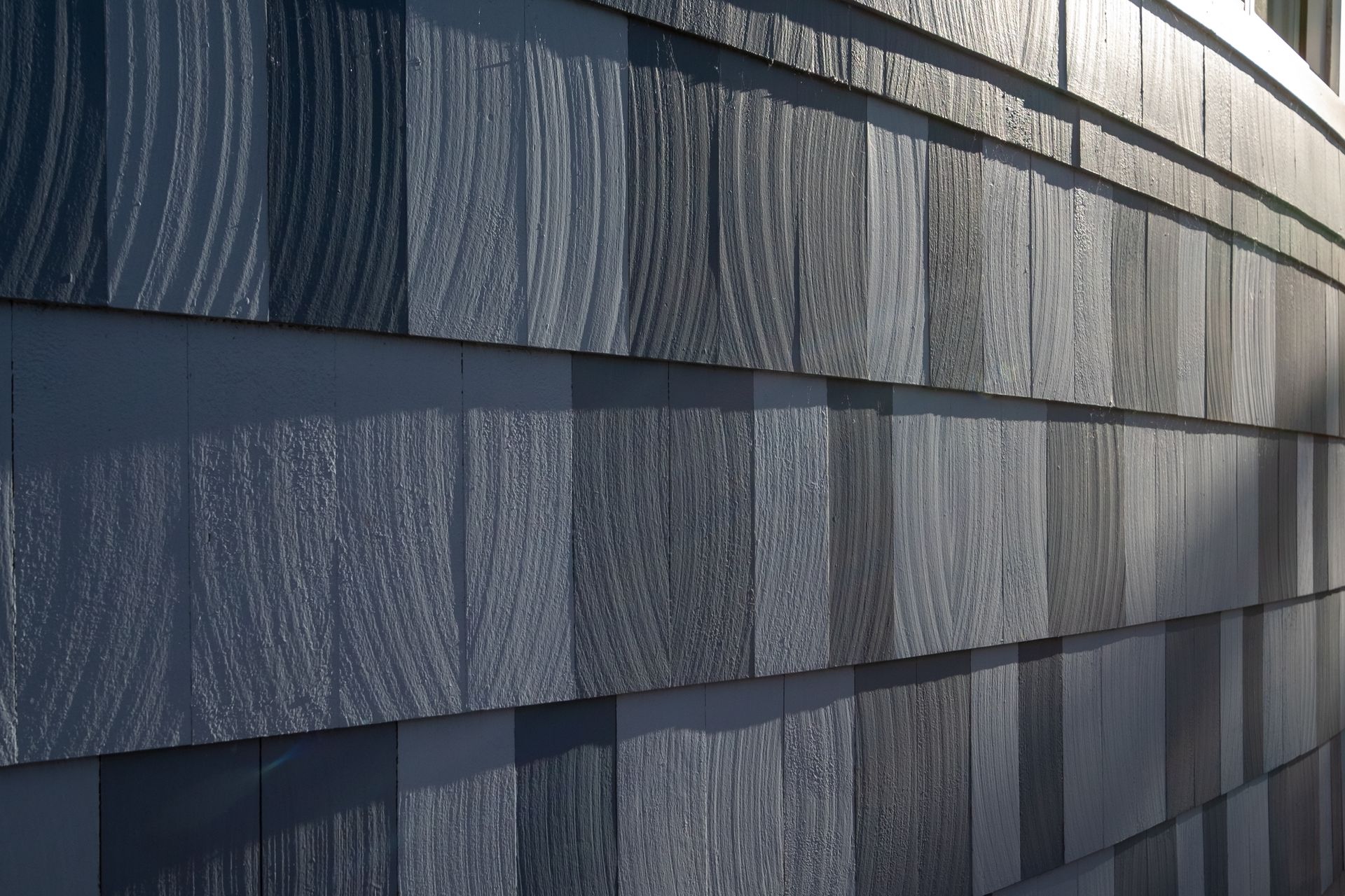Close-up of gray shingled siding with layered rectangular tiles and textured wood grain