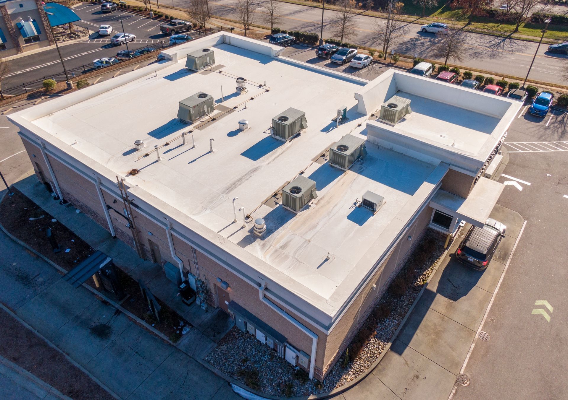 Aerial view of a white-roofed commercial building with HVAC units and parking lot nearby