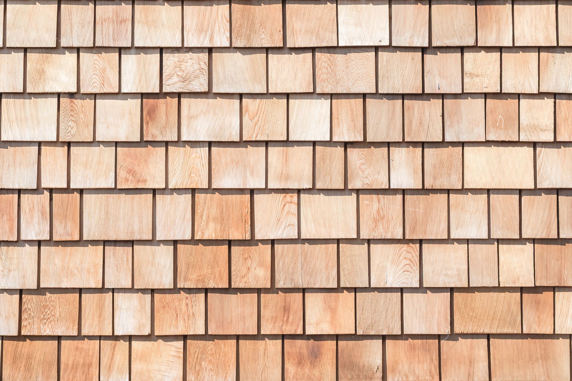 Stacked beige and tan wooden shingles arranged in horizontal rows on a wall.