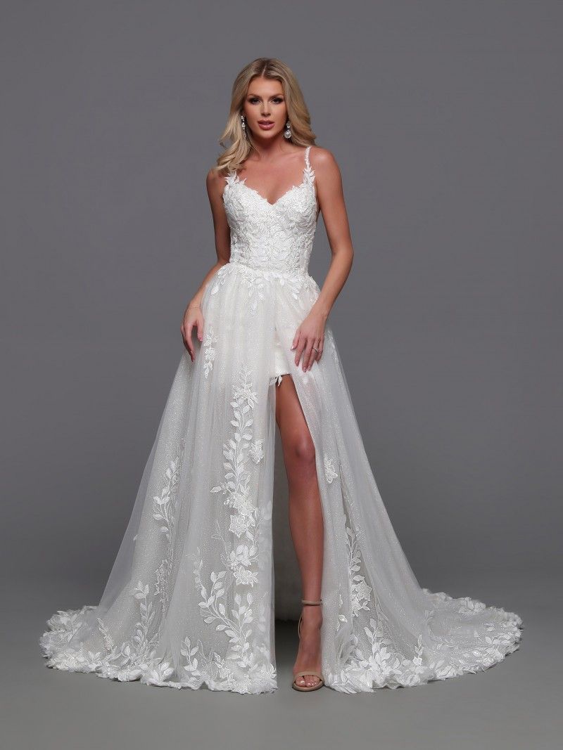 Woman in white wedding dress with high slit, standing against a gray backdrop.