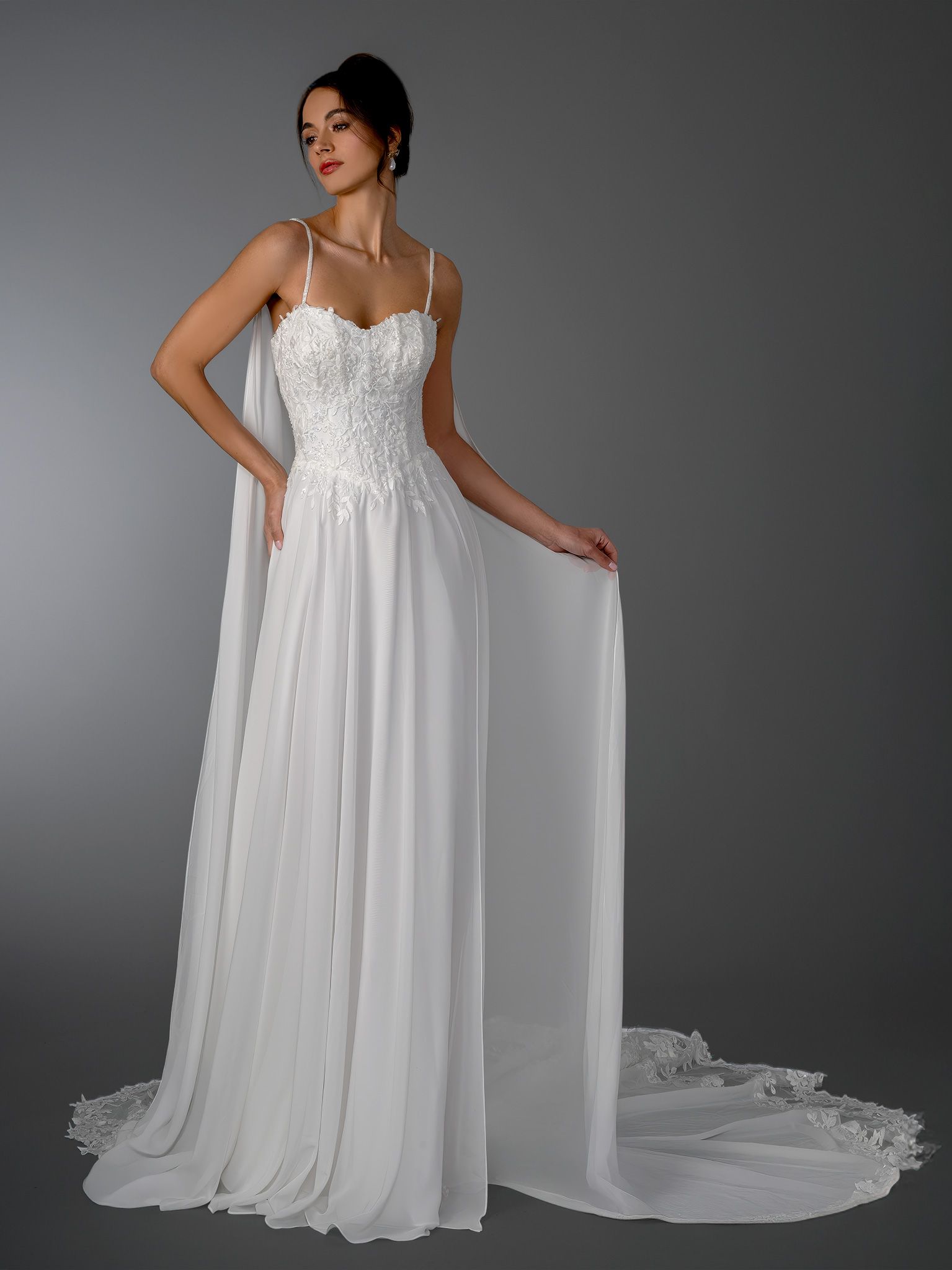 Woman in white wedding dress with flowing cape, holding a fabric edge.