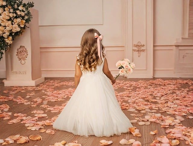 Girl in a white dress, holding flowers, surrounded by rose petals, facing away.