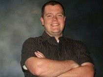 A man in a striped shirt is standing with his arms crossed and smiling.
