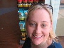 A woman is smiling in front of a display of snacks.