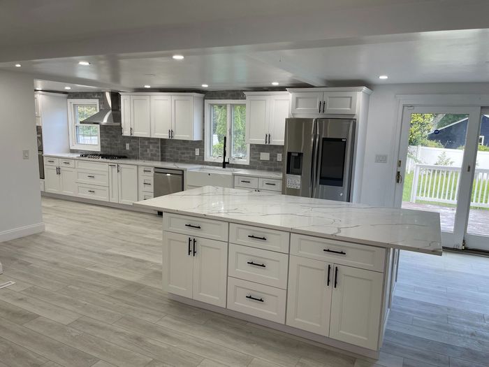 Modern white kitchen with island, stainless steel appliances, and gray tile backsplash.