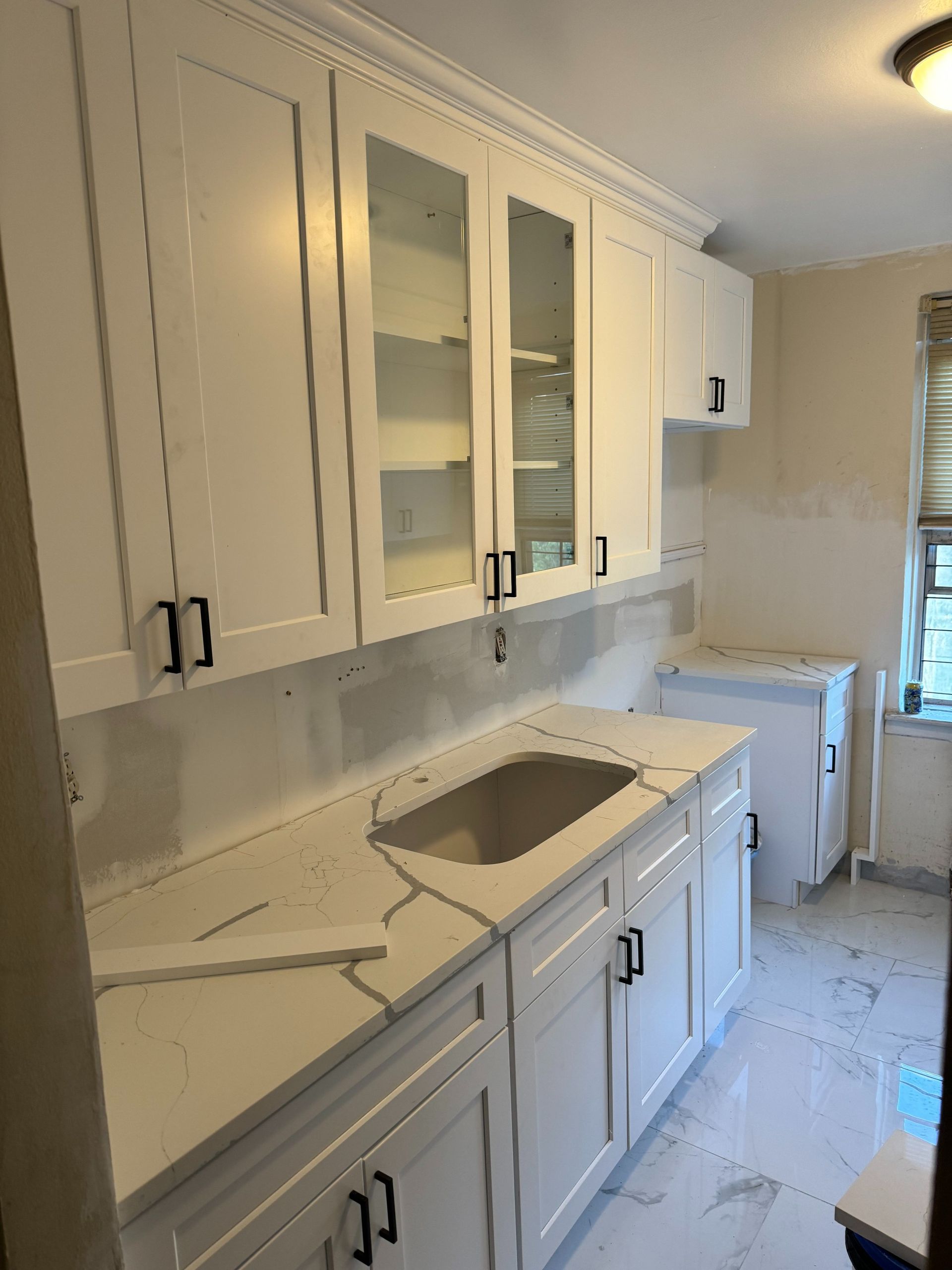 White kitchen cabinets with black handles, a white countertop, and a built-in sink.