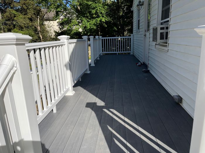 White deck with gray flooring, railing, and exterior wall of a building.