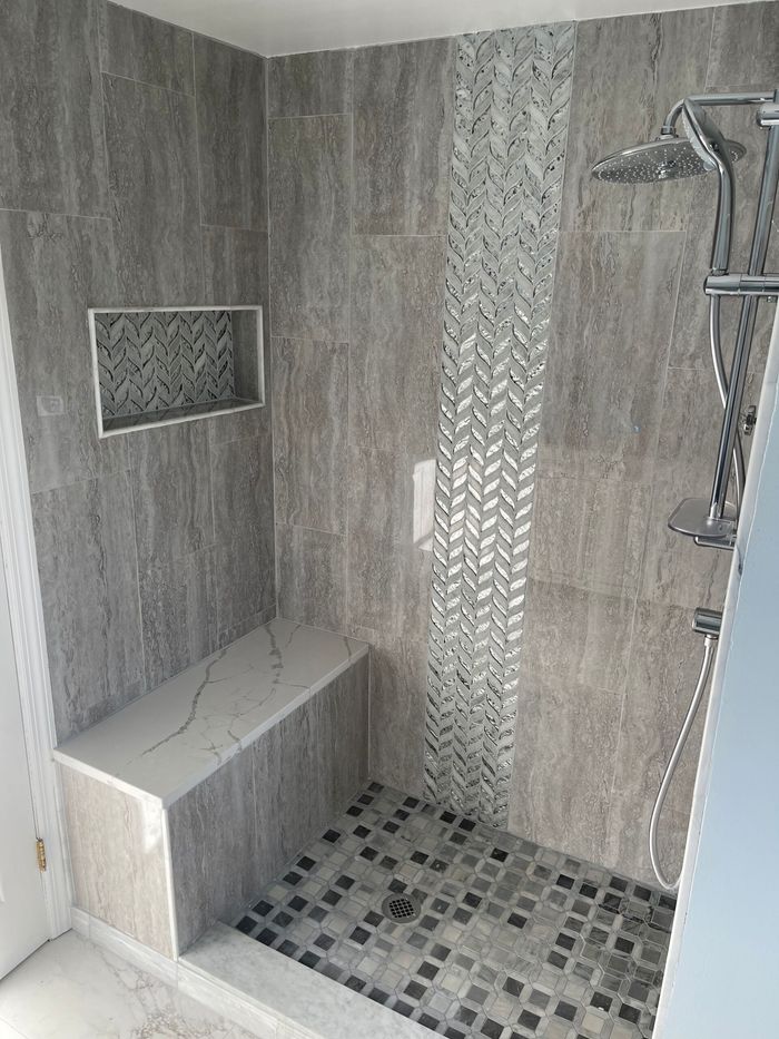 Gray tiled shower with a built-in bench, niche, and mosaic accent strip.