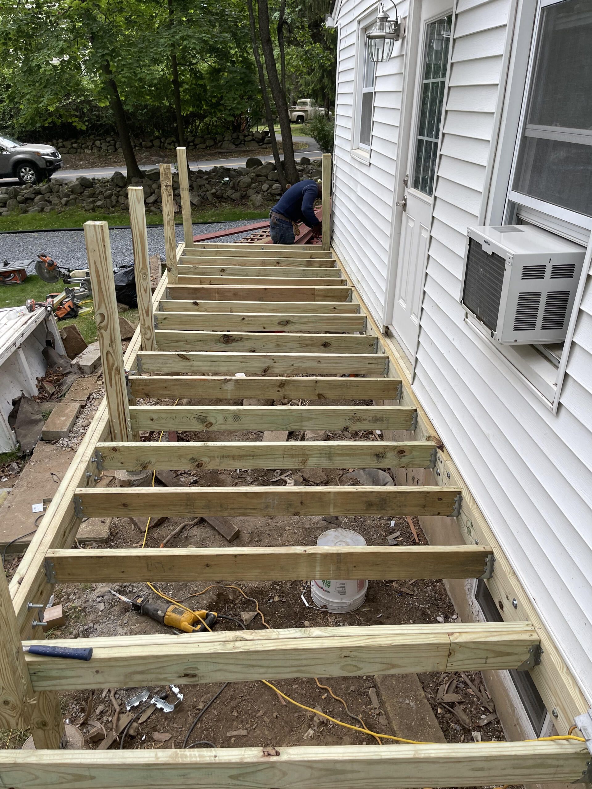 Wooden staircase under construction beside a white house, person working on the top step.