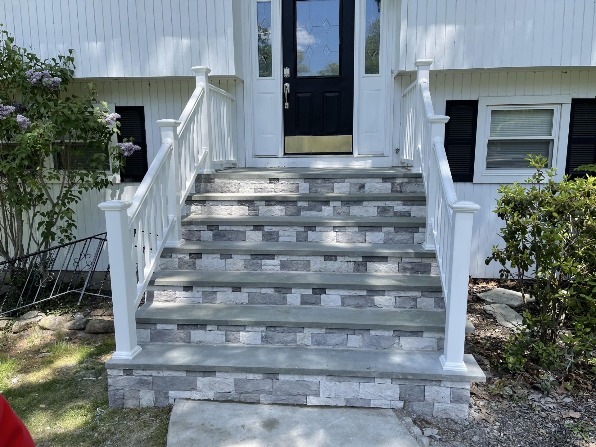 White house entrance with stone steps, white railings, and a black door.