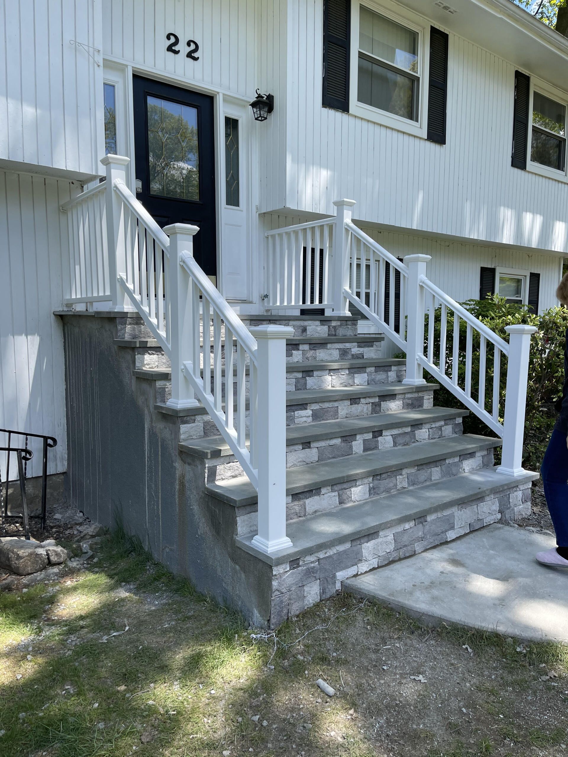 Exterior of a house with a concrete and stone staircase and white railing leading to the front door.