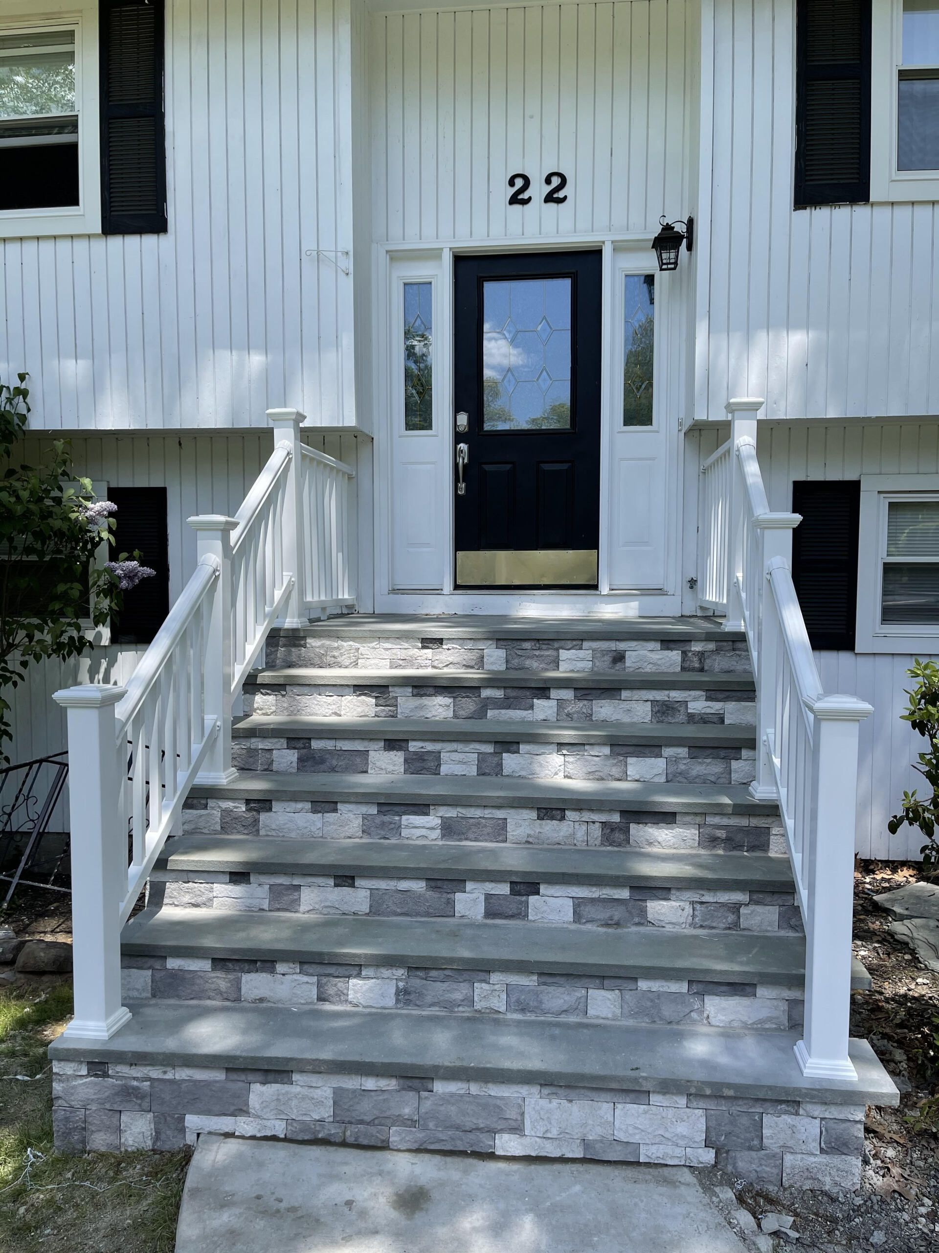White house entrance with stone steps, a black door, and white railing. Number 22 above door.