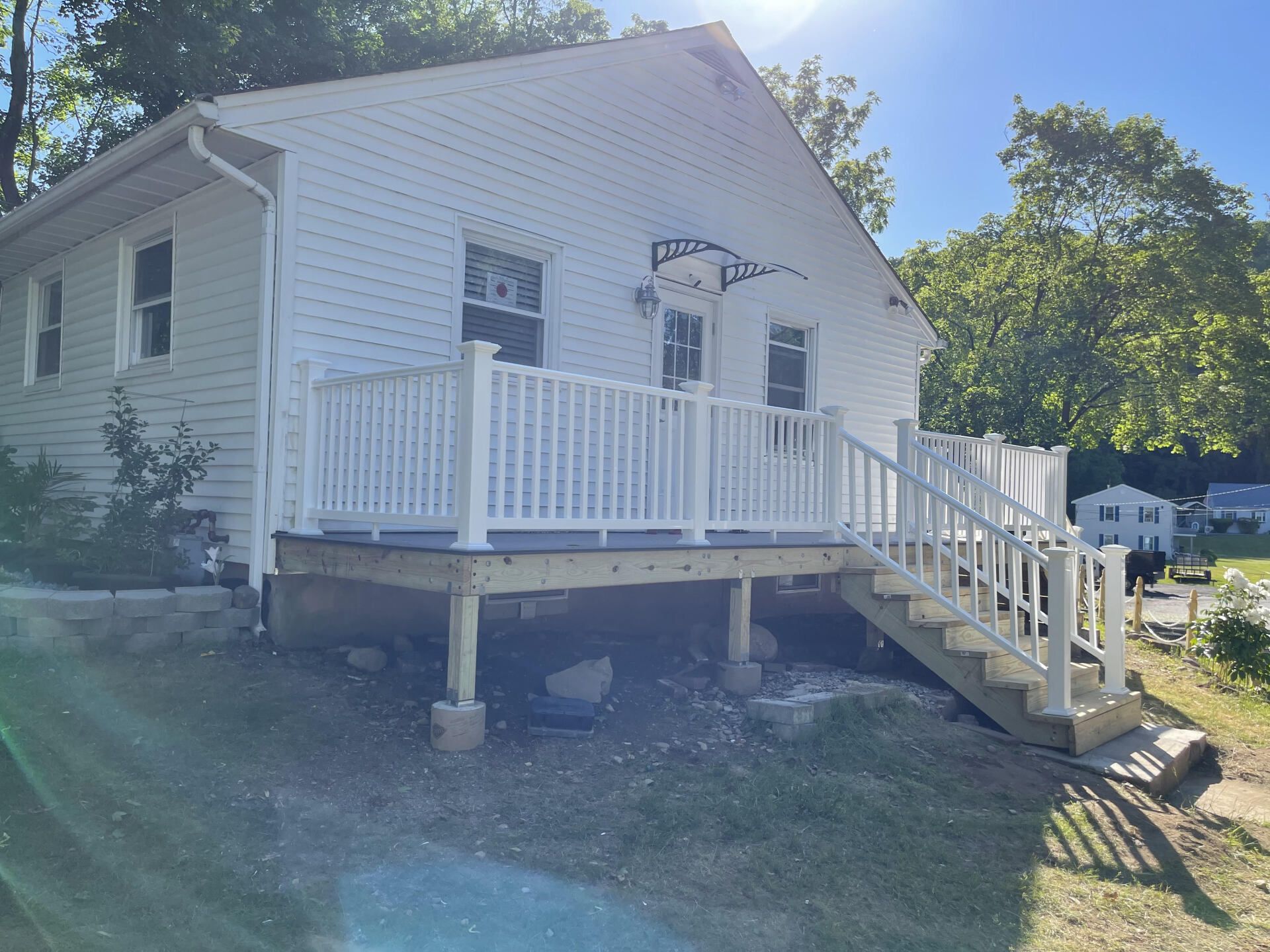White house with white railing deck, stairs, and awning over door; green grass.