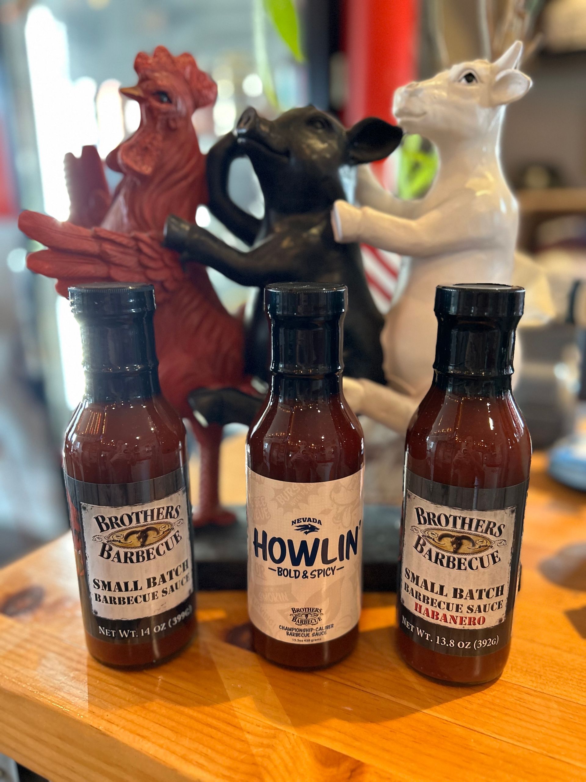 Three bottles of barbecue sauce are sitting on a wooden table.