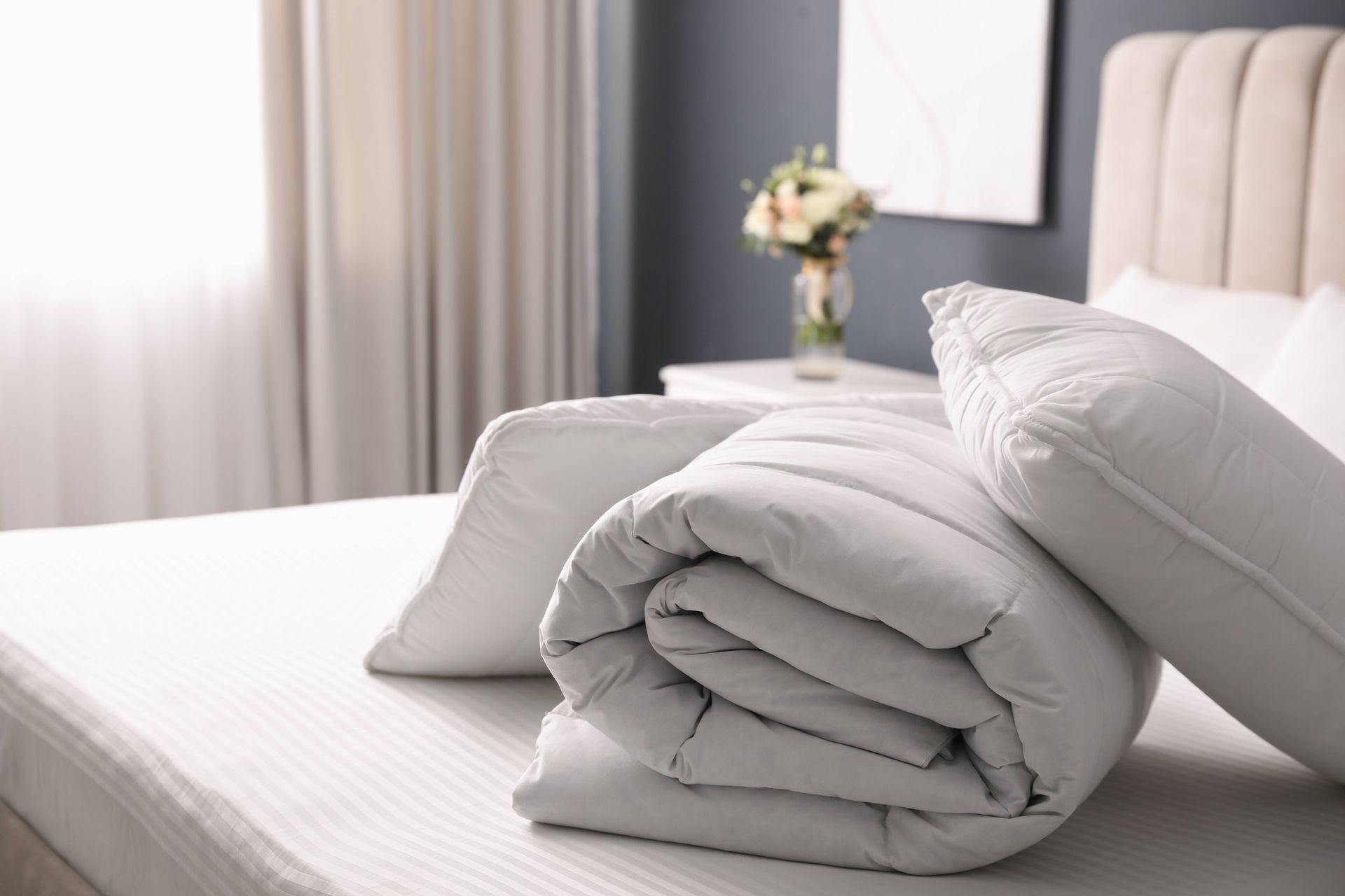 A bed with a rolled up comforter and pillows on it.