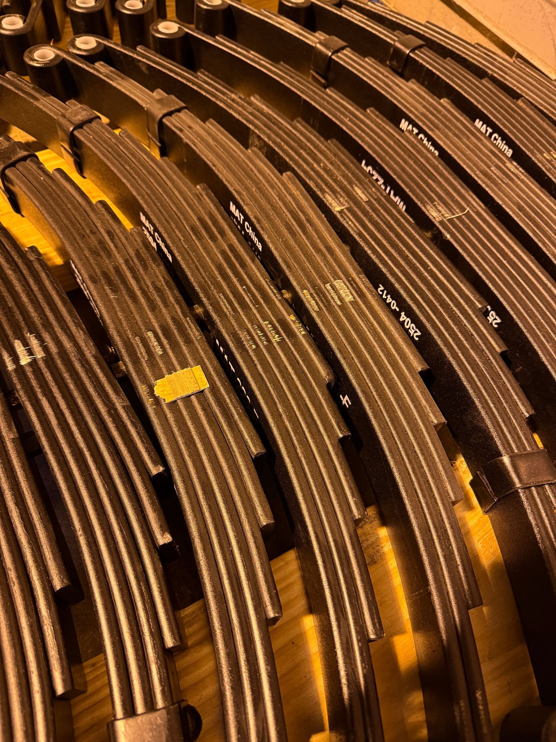 A collection of several curved, stacked black metal leaf springs arranged side-by-side on a yellow surface.