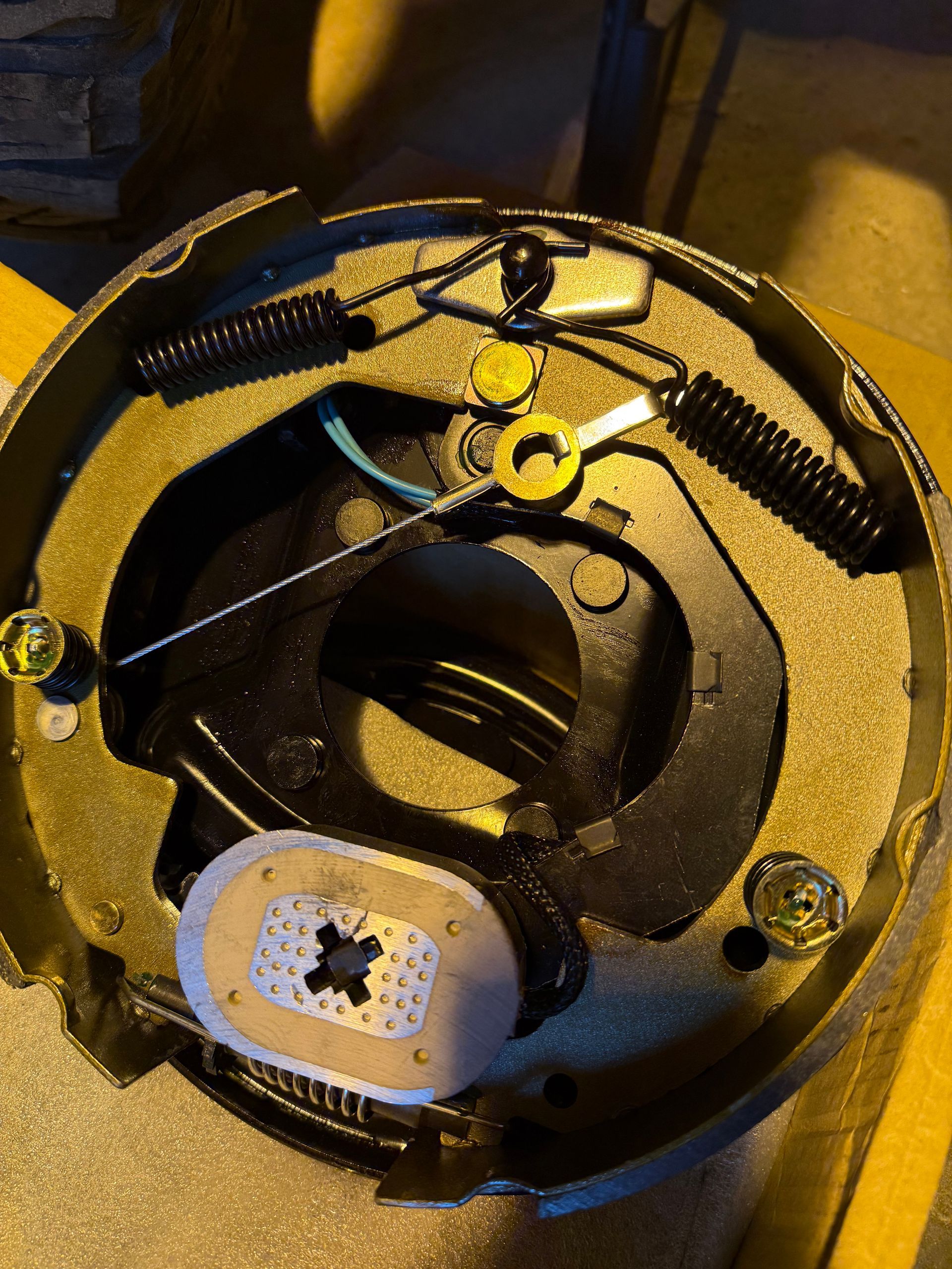 A drum brake assembly with curved metal shoes, springs, and a central adjustment mechanism on a dark backing plate.