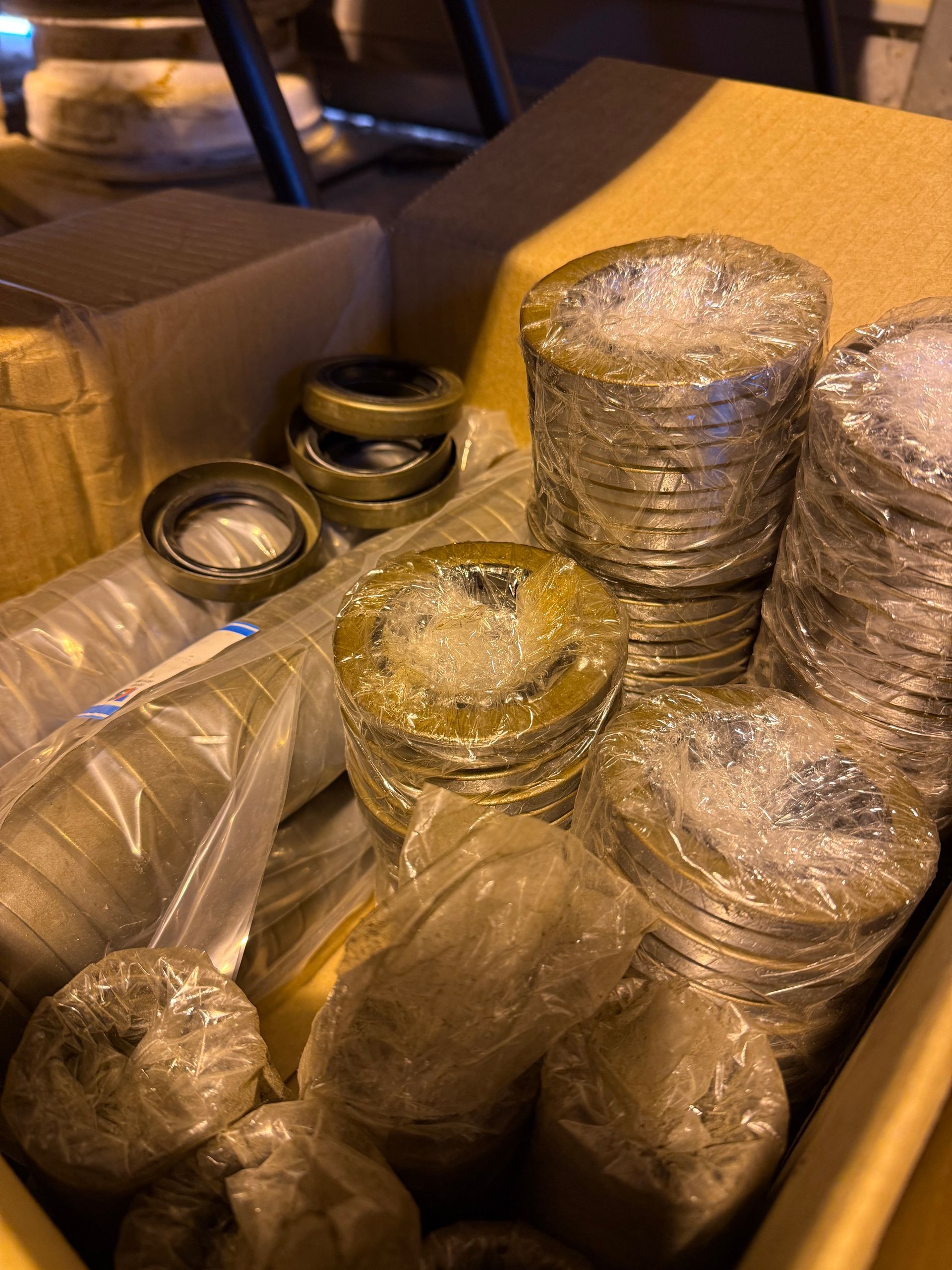 A cardboard box filled with several stacks of wrapped metal gaskets and loose seals.