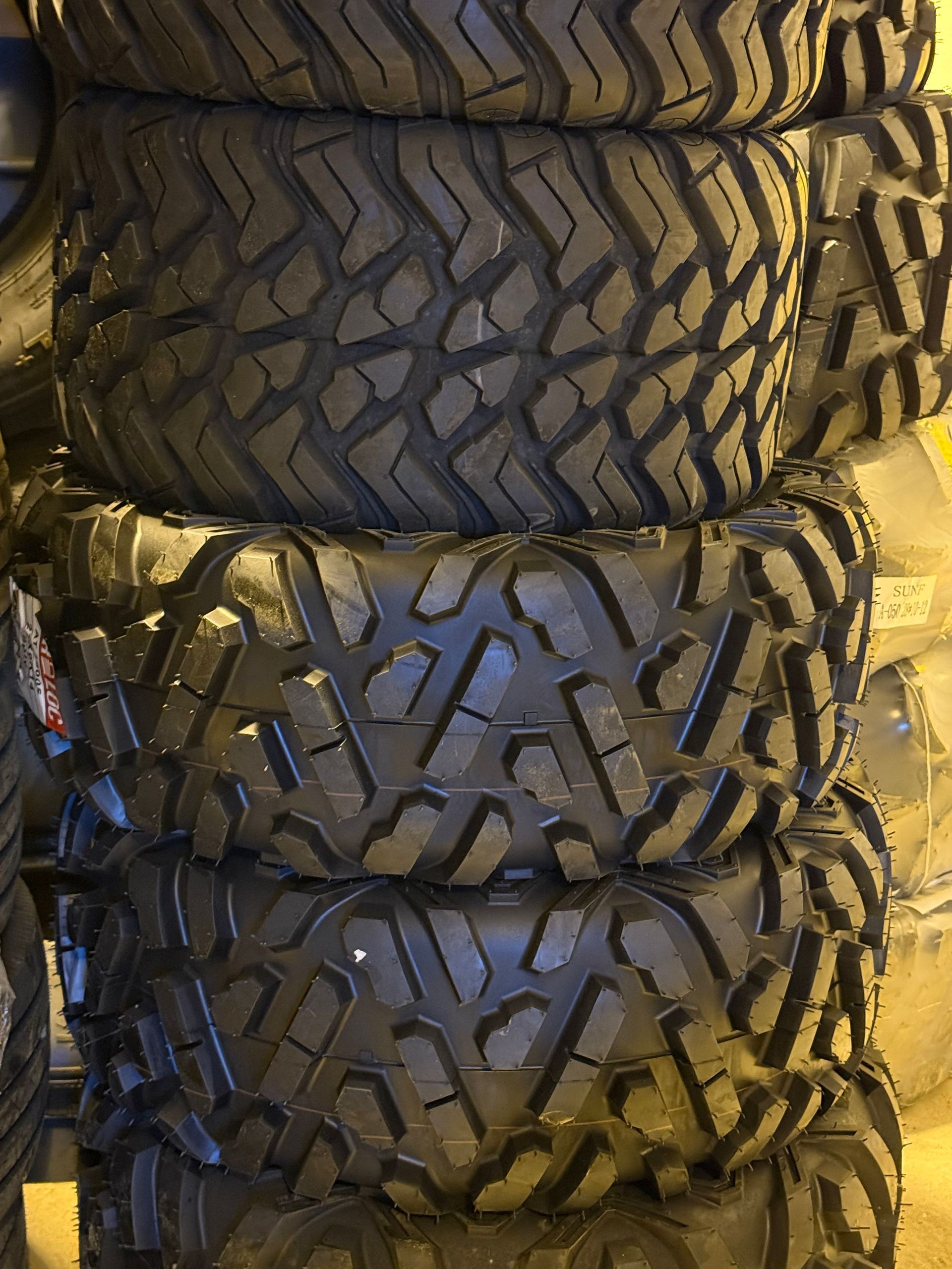 A stack of black off-road tires with rugged, deep-grooved tread patterns.